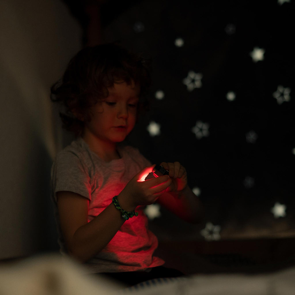 Child holding a glowing red headlamp in a dark room