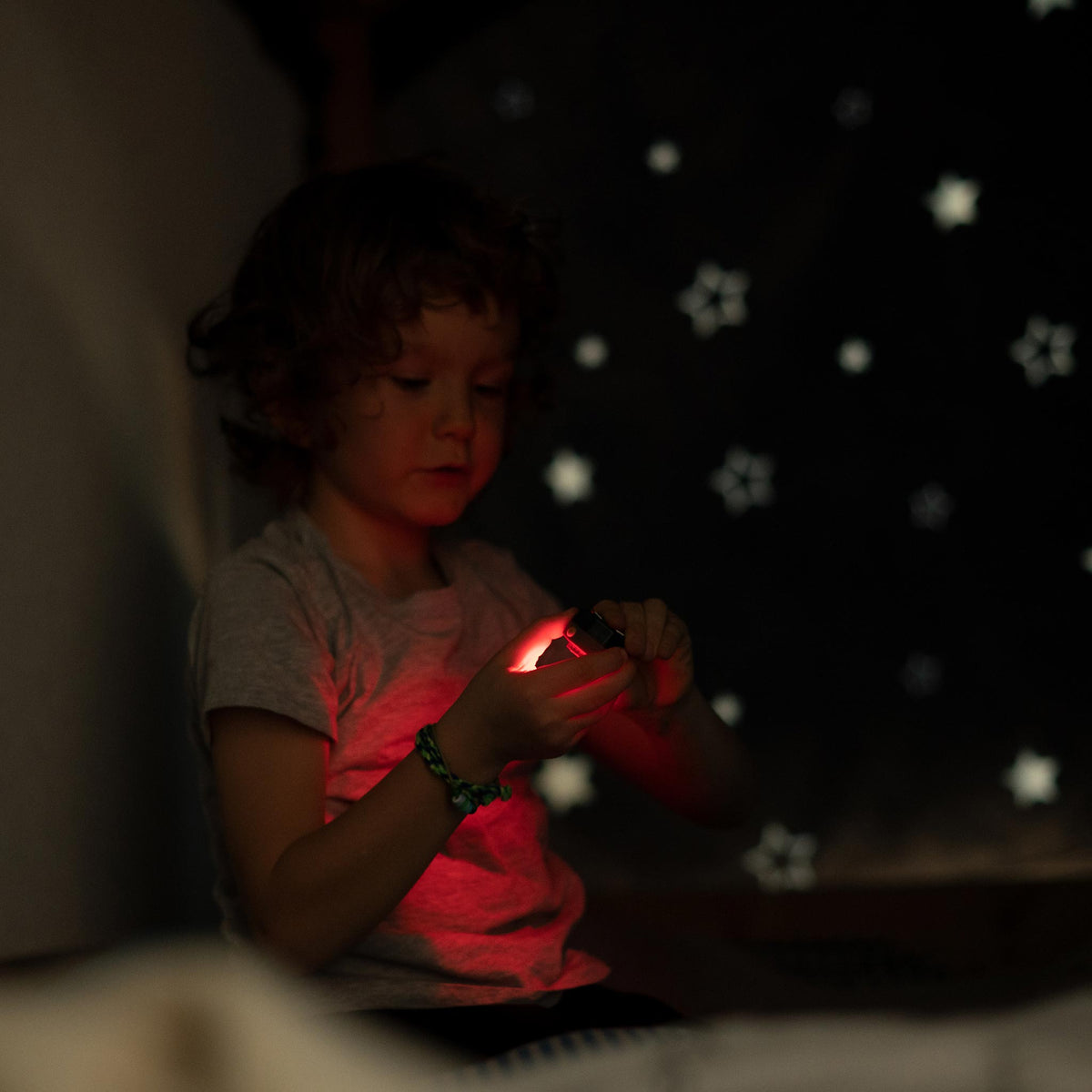 Child holding a glowing red headlamp in a dark room
