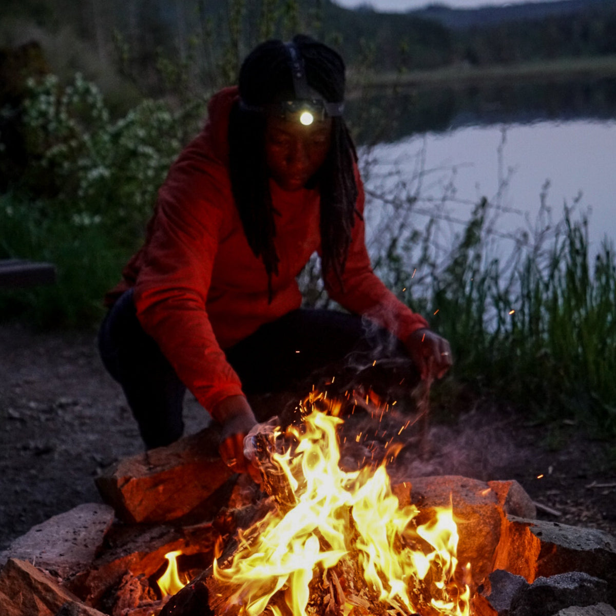 Outdoor headlamp with bright beam on a red jacket near a campfire