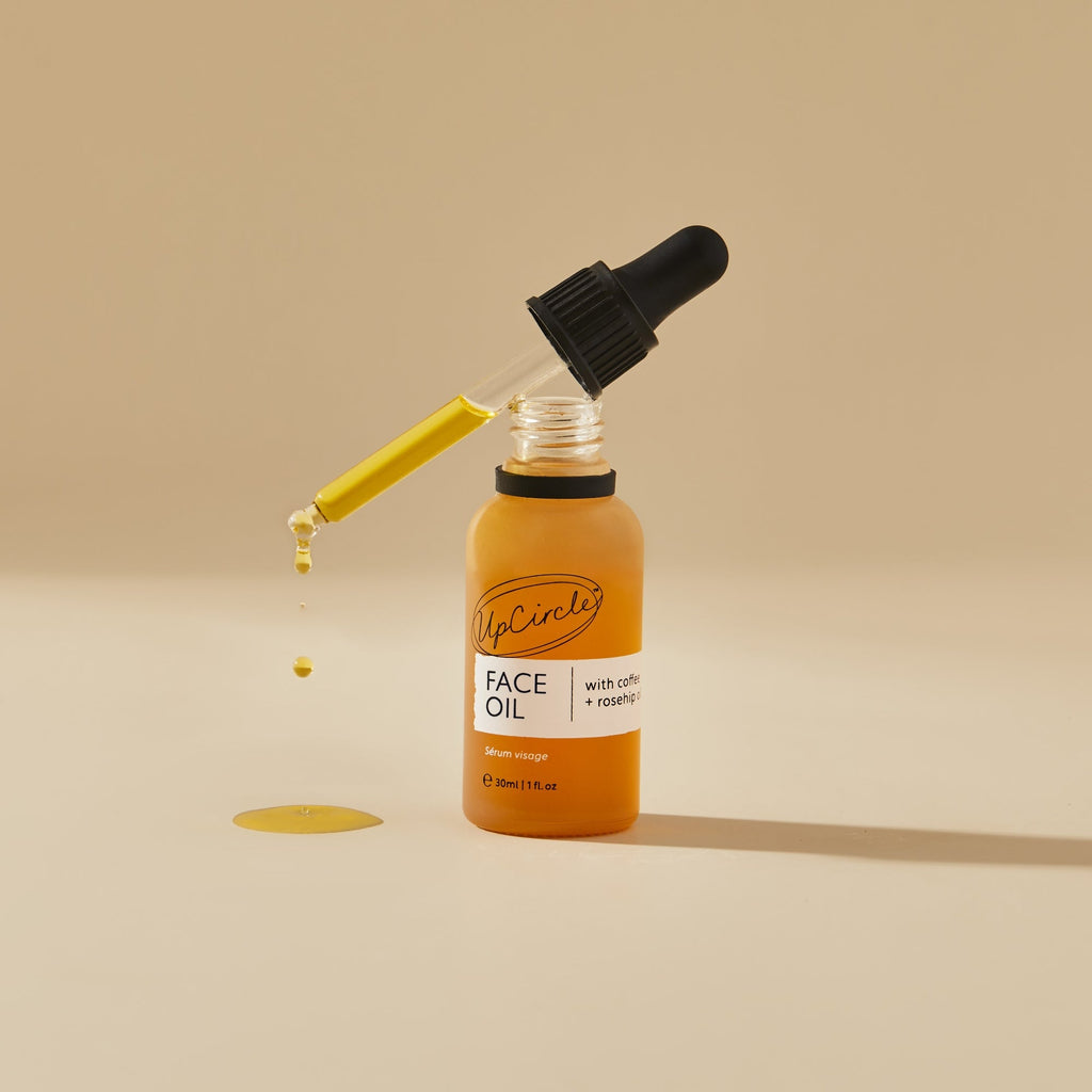 Face oil bottle with black dropper dispensing a drop onto the surface