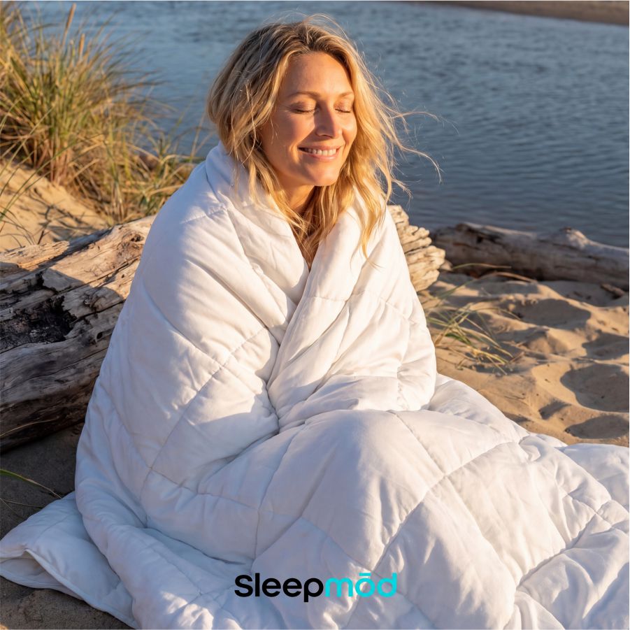 White comforter on sand with person relaxing outdoors