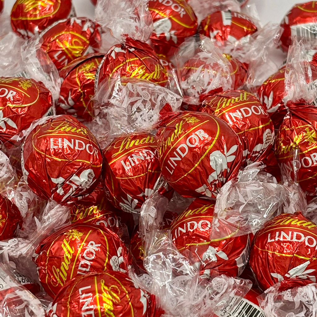 Close-up pile of red Lindt LINDOR milk chocolate truffles in crinkled white wrappers.