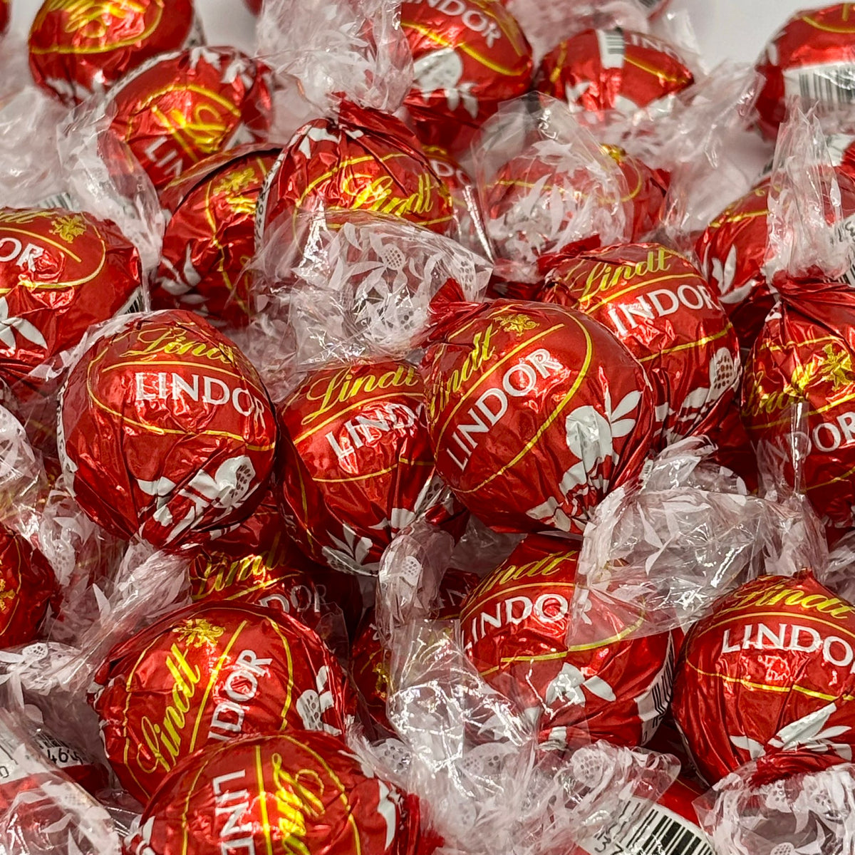 Close-up pile of red Lindt LINDOR milk chocolate truffles in crinkled white wrappers.