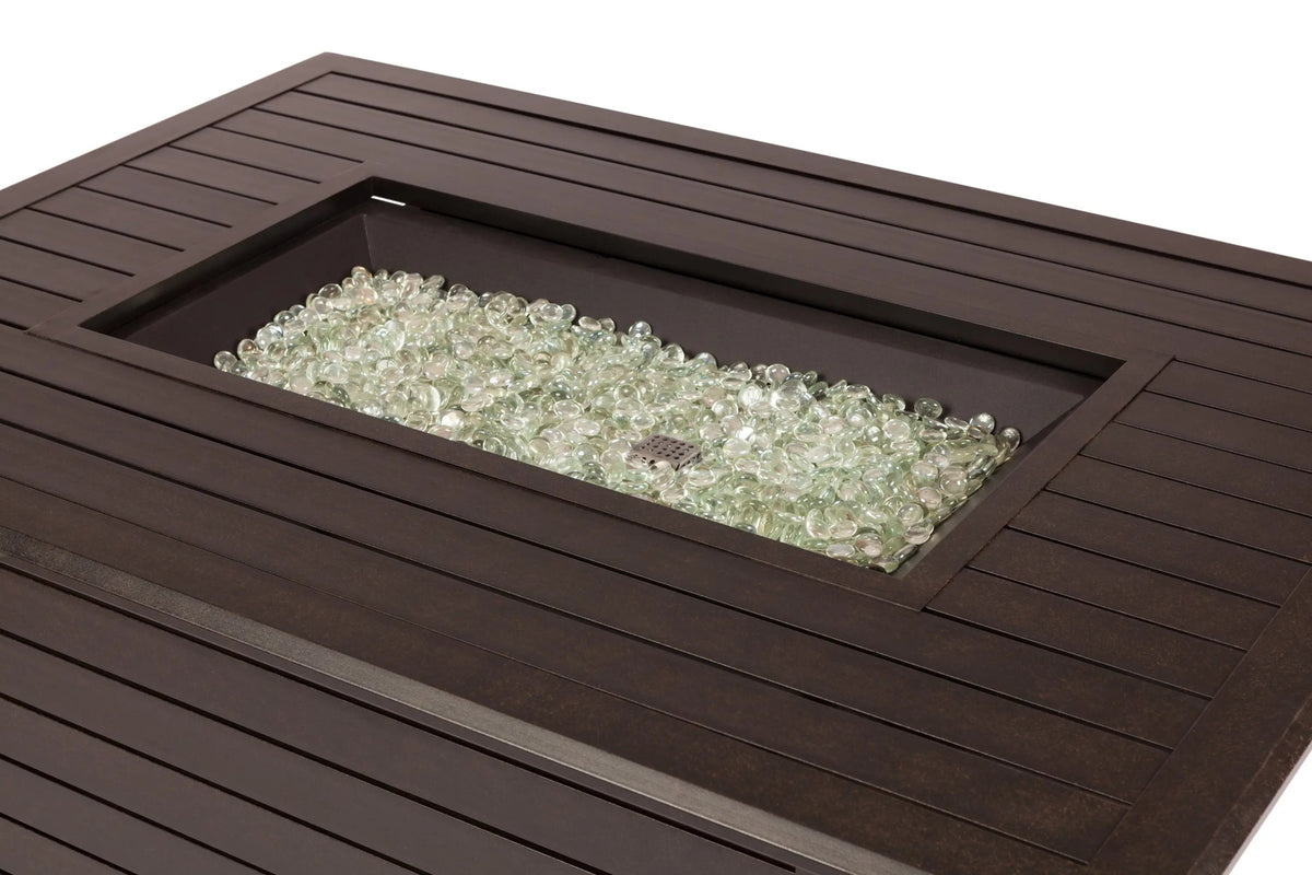Open fire pit tray filled with clear glass fire media in a dark rectangular table.