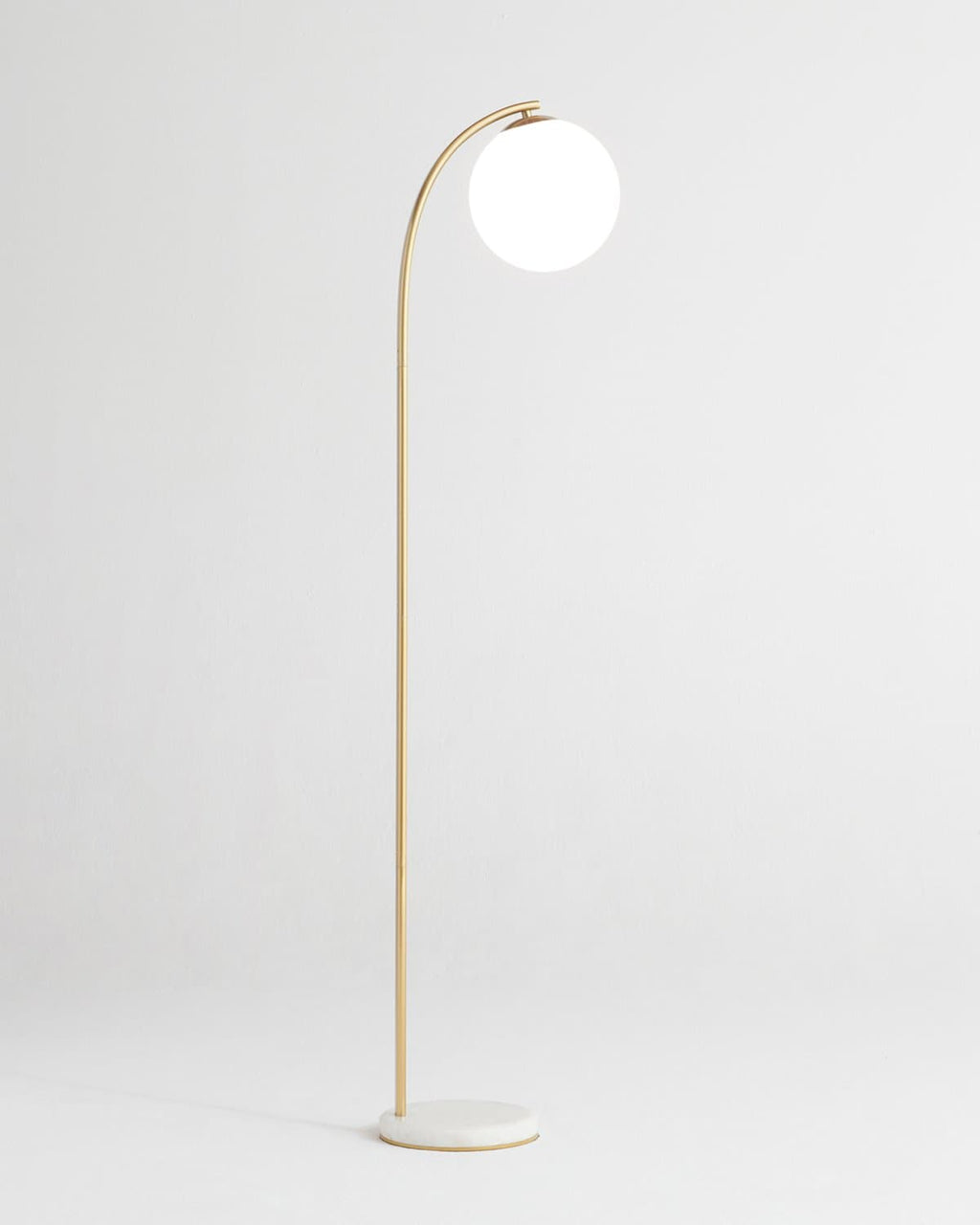Gold arched floor lamp with round white globe shade, side view