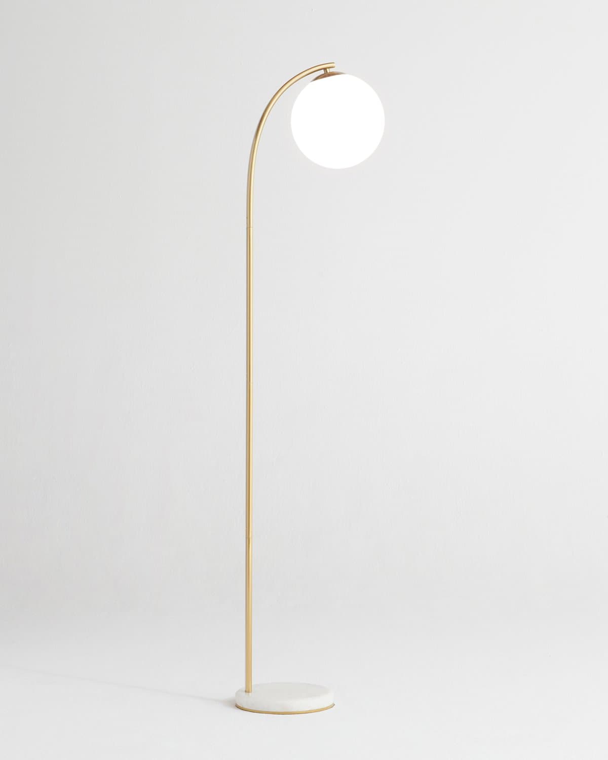 Gold arched floor lamp with round white globe shade, side view