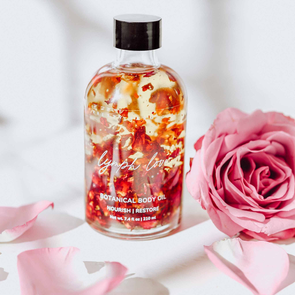 Amber botanical body oil bottle with black cap beside pink roses.