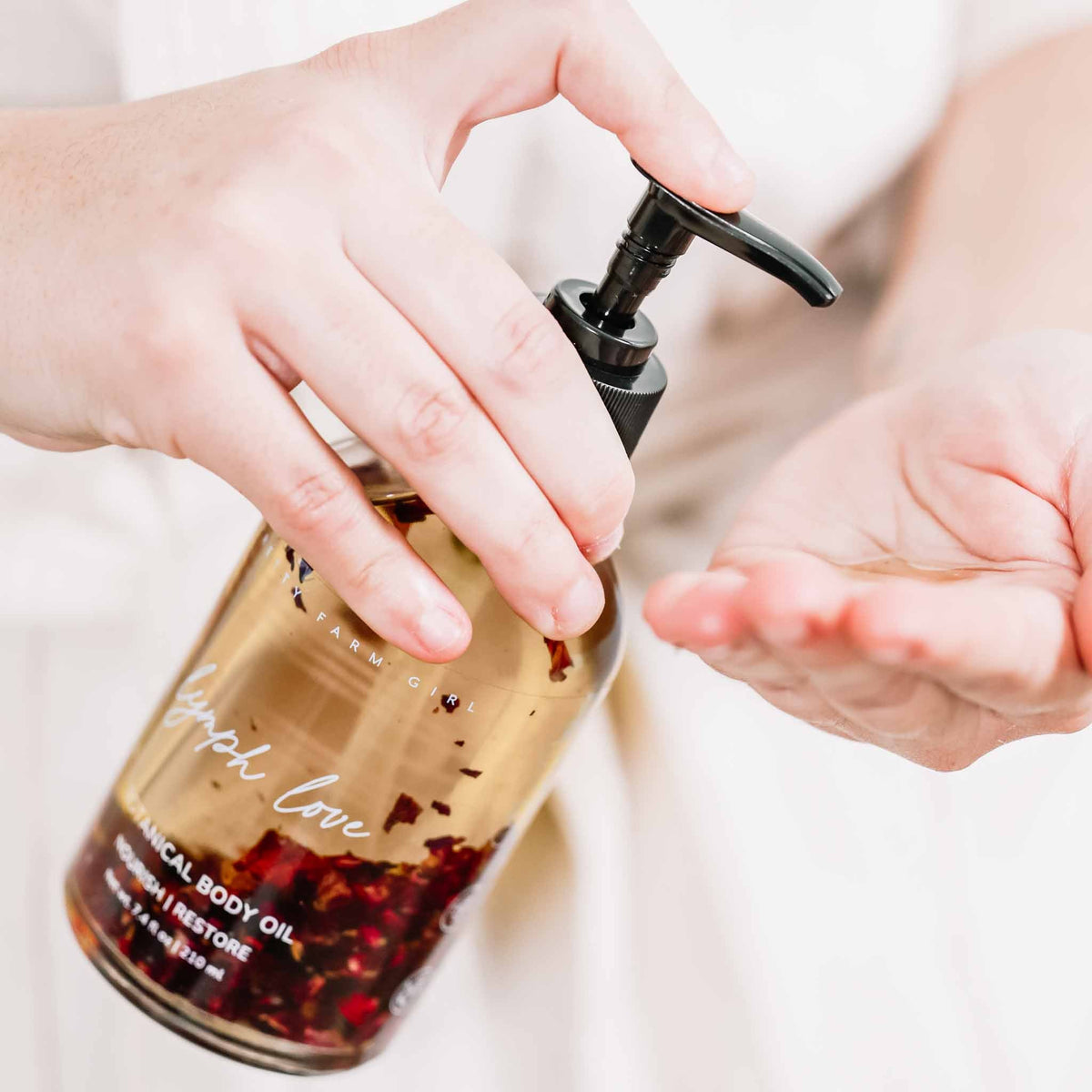 Hands using an oil pump bottle with a glass body oil container