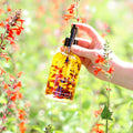 Amber botanical body oil bottle with black pump, held near orange blossoms.
