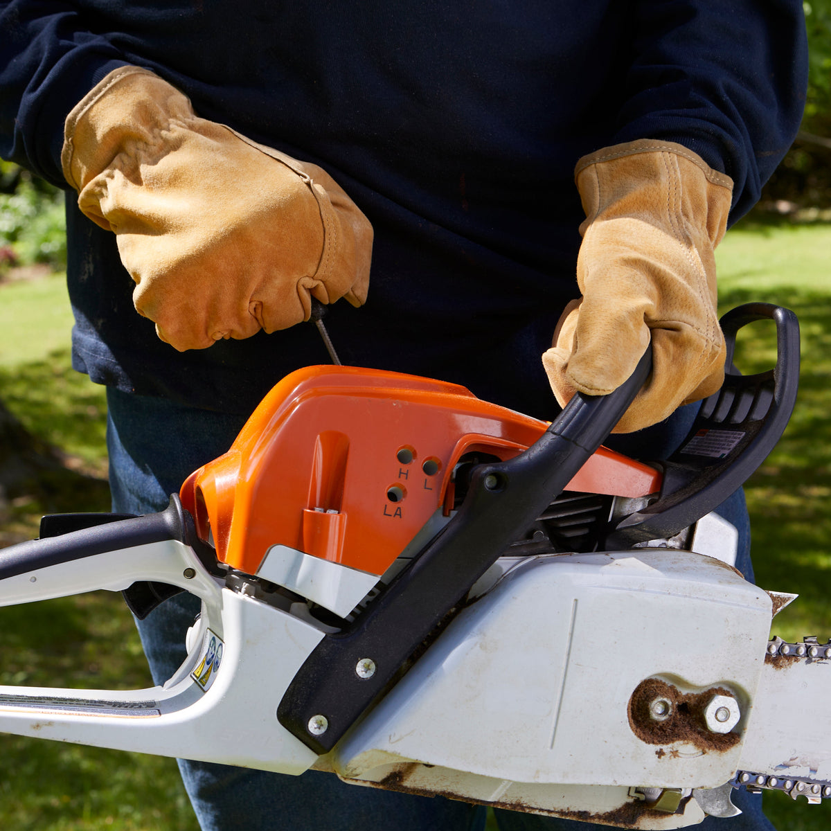 Tan leather work gloves on chainsaw handles; stitched cuffs visible.