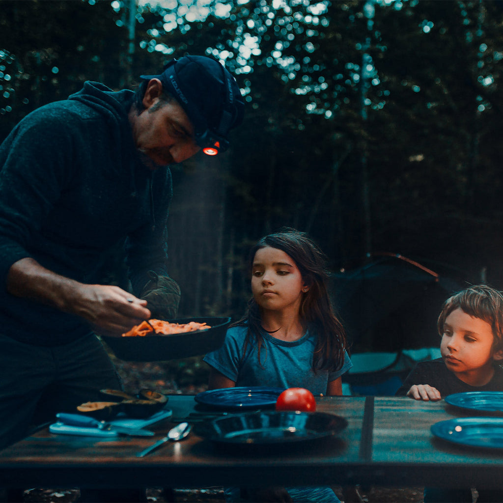 Outdoor headlamp glowing warm light while cooking near a campsite