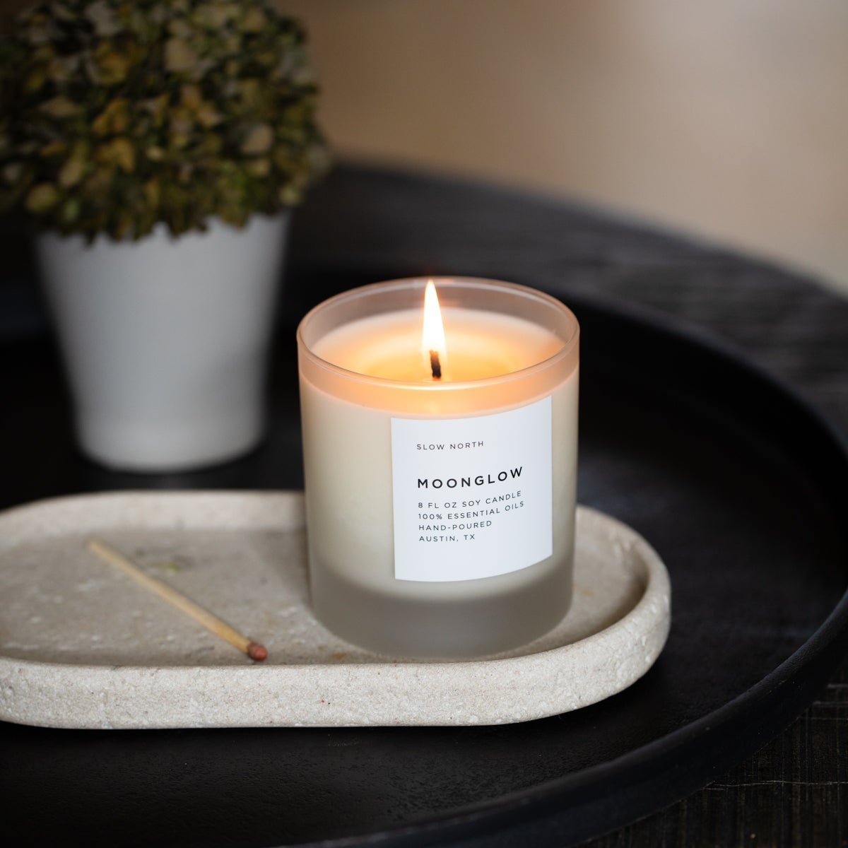 Moonglow scented candle in frosted jar with burning wick on stone coaster
