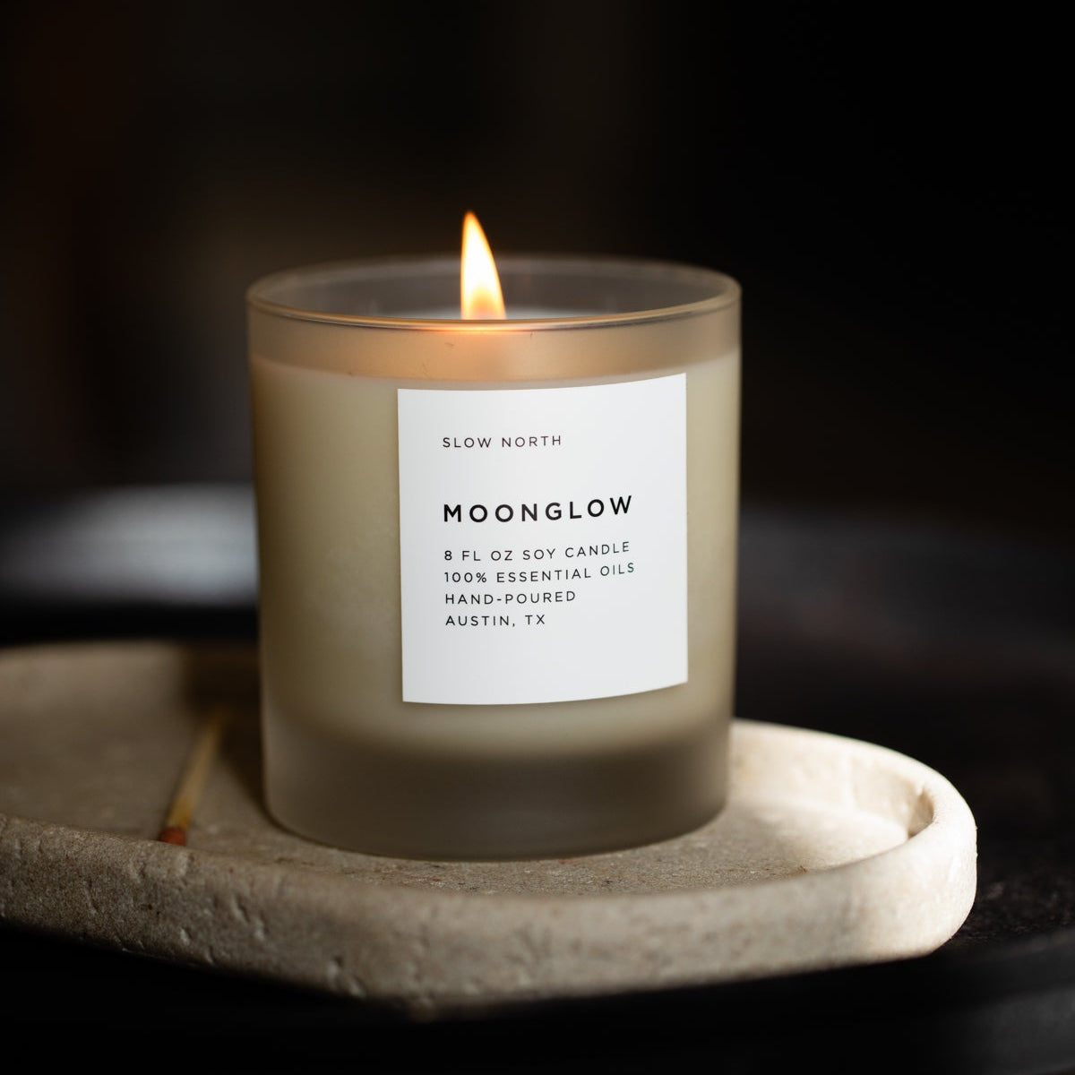 Moonglow scented candle in clear glass jar with burning wick on stone tray