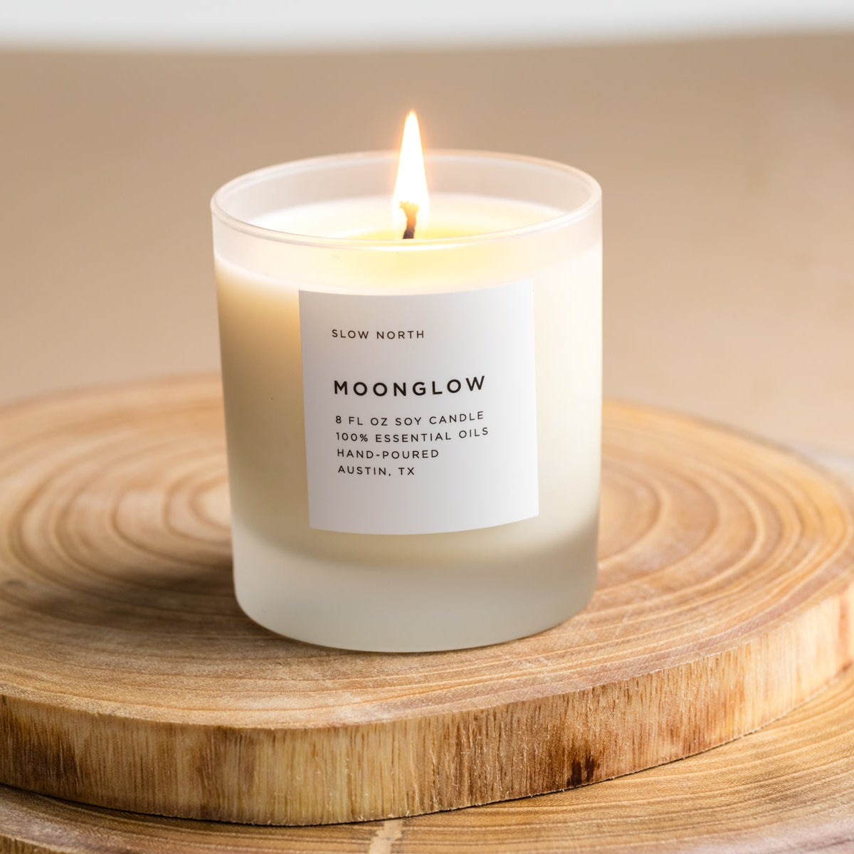 Moonglow scented candle in frosted jar with burning wick on wooden board