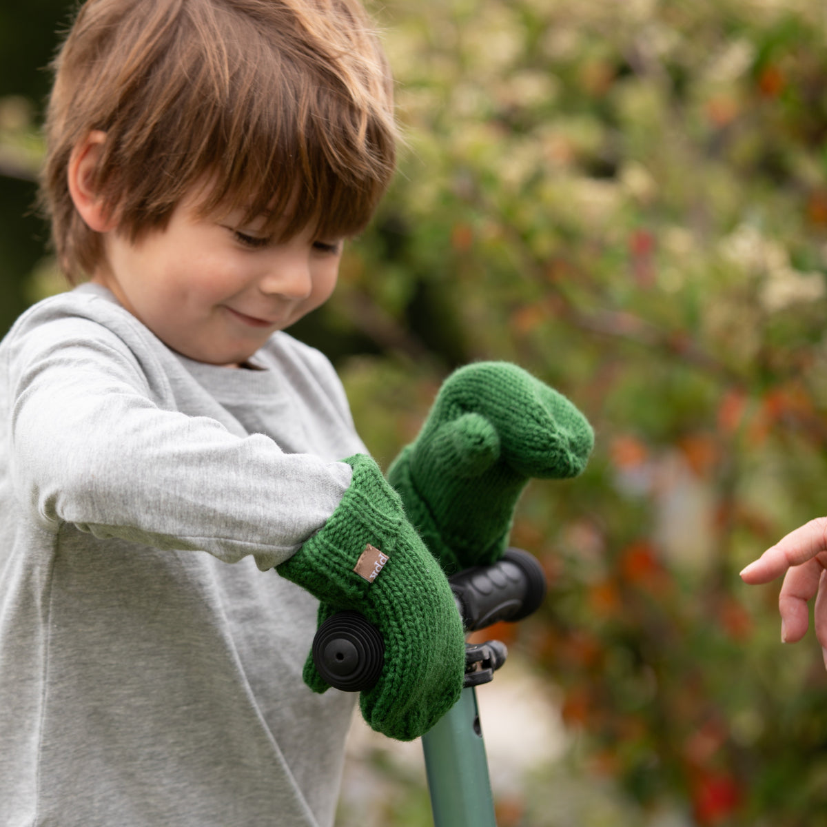 Forest green knit mittens on a child’s hands outdoors, holding a handle