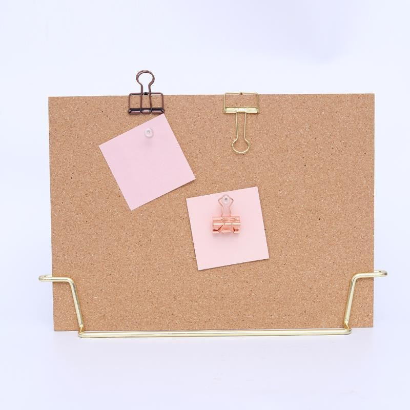 Standing cork bulletin board with gold metal clips and pins, holding pink notes