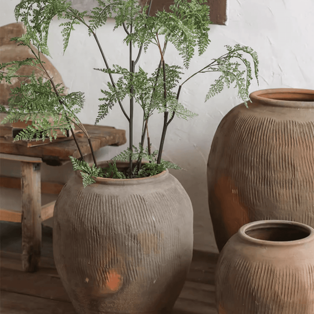 Brown ribbed earthenware round vase pot with wide opening and tall greenery