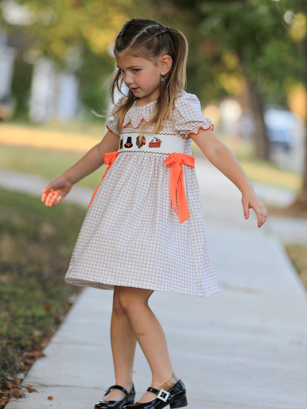 Girls gingham Thanksgiving dress viewed from side, orange ribbon bows at waist