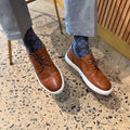 Men's cognac wingtip lace-up shoes with white soles, worn with blue pants