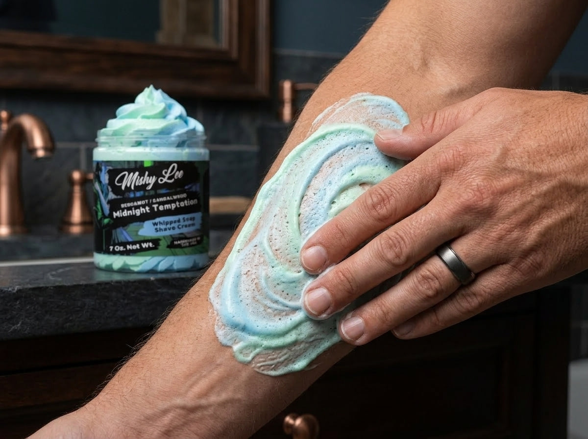 Hand lathering mint and blue whipped shave cream on skin with Mishy Lee jar in back