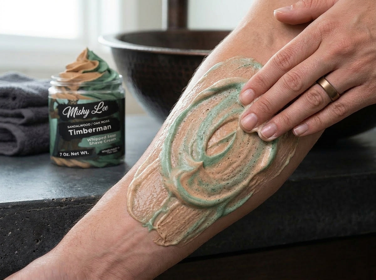 Whipped soap and shave cream swirled onto forearm; jar and teal-tan lather visible