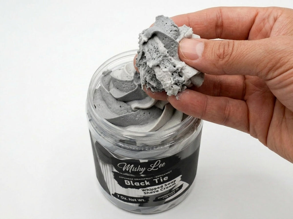 Hand holding a clump of gray whipped soap from a whipped shave cream jar