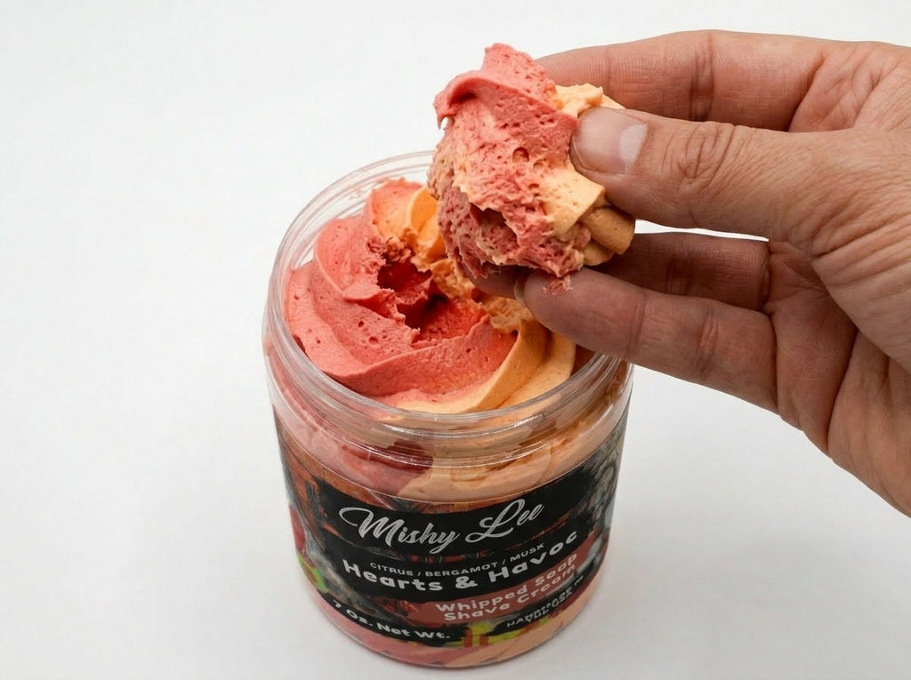 Hand holding a scoop of whipped soap and shave cream from jar, pink and orange swirls