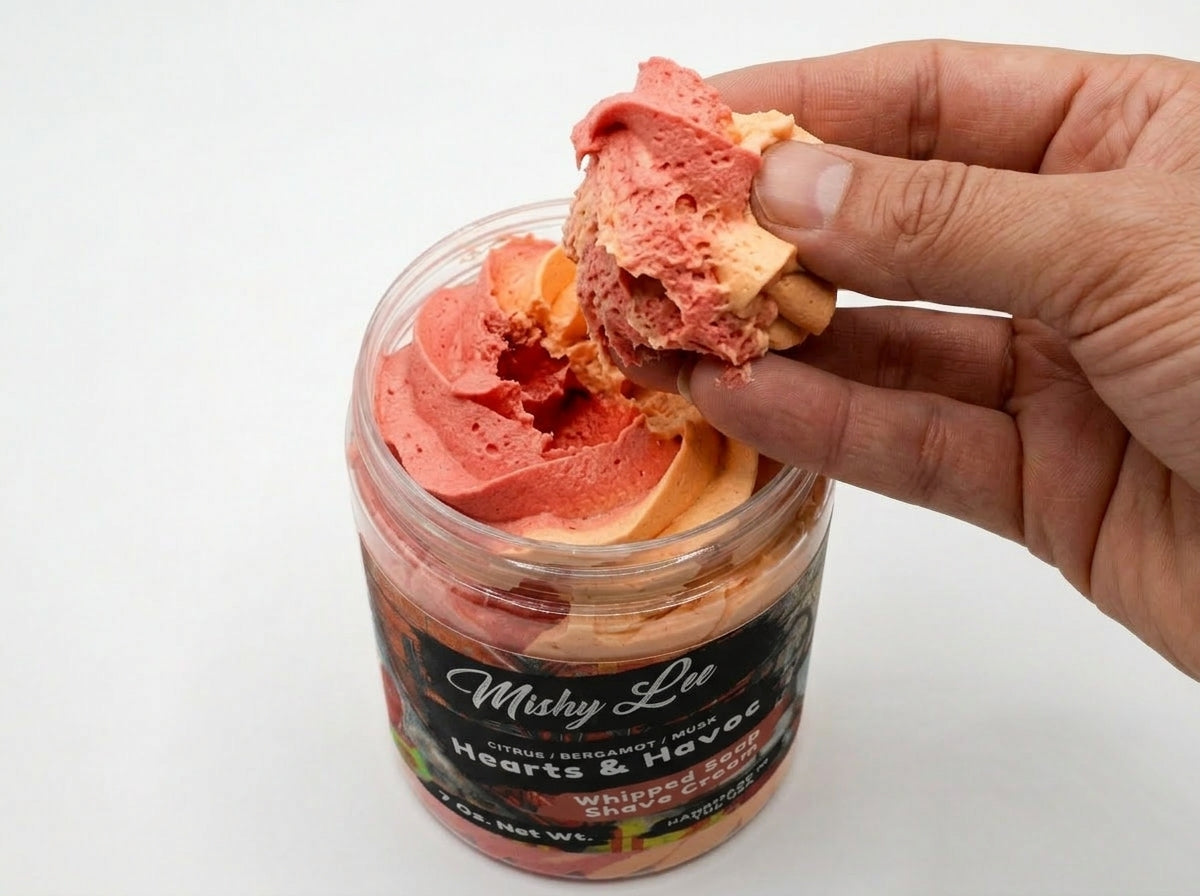 Hand holding a scoop of whipped soap and shave cream from jar, pink and orange swirls