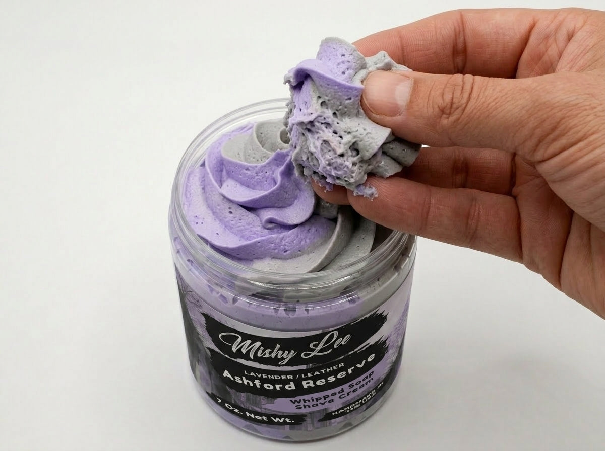 Hand holding a scoop of purple whipped soap/shave cream over open jar