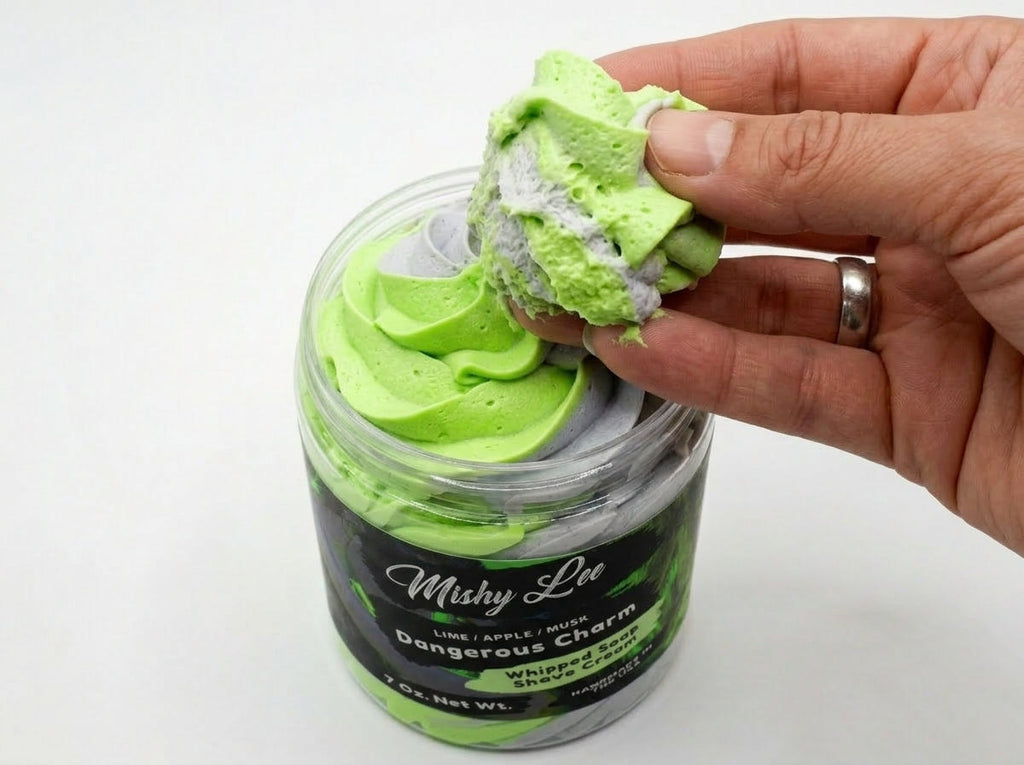 Hand holding a scoop of green whipped soap with gray layers from jar