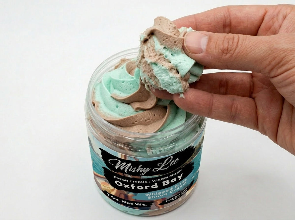 Hand holding a scoop of whipped soap and shave cream from teal and tan swirl jar