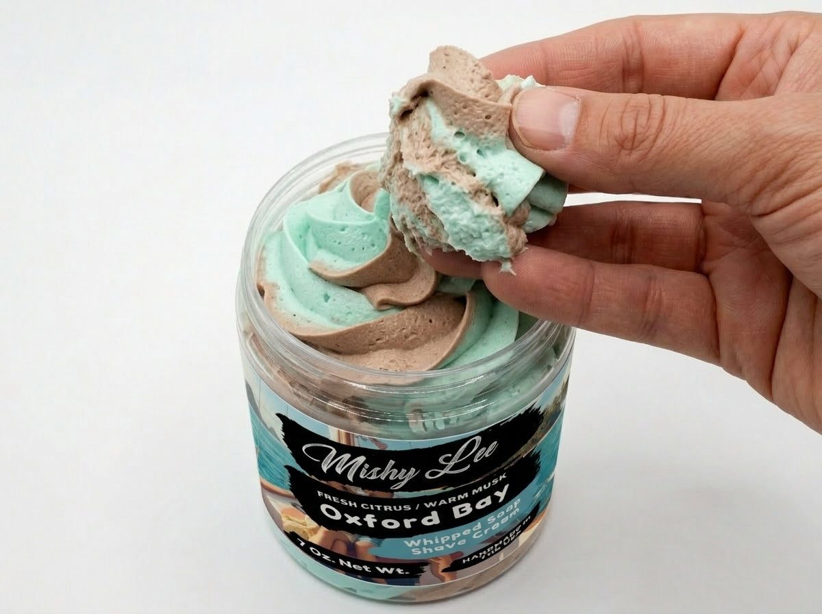Hand holding a scoop of whipped soap and shave cream from teal and tan swirl jar