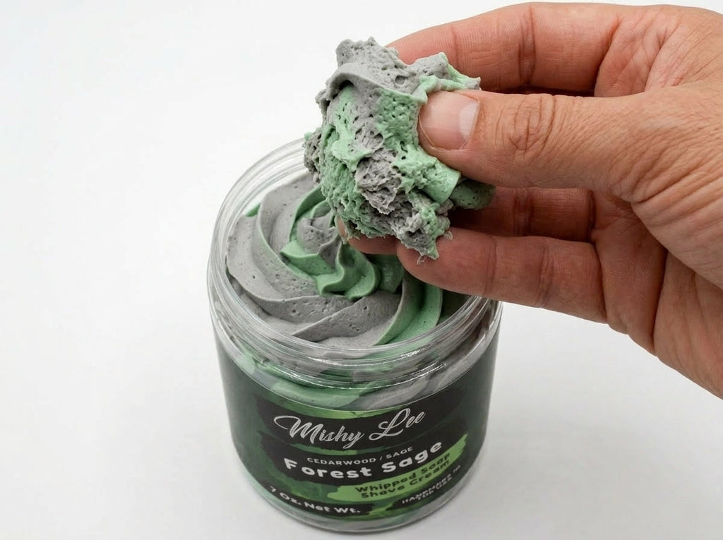 Hand holding a scoop of green whipped soap and shave cream from the jar