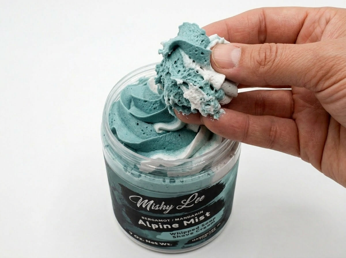 Hand holding scoop of turquoise whipped soap from a men’s shave cream jar.