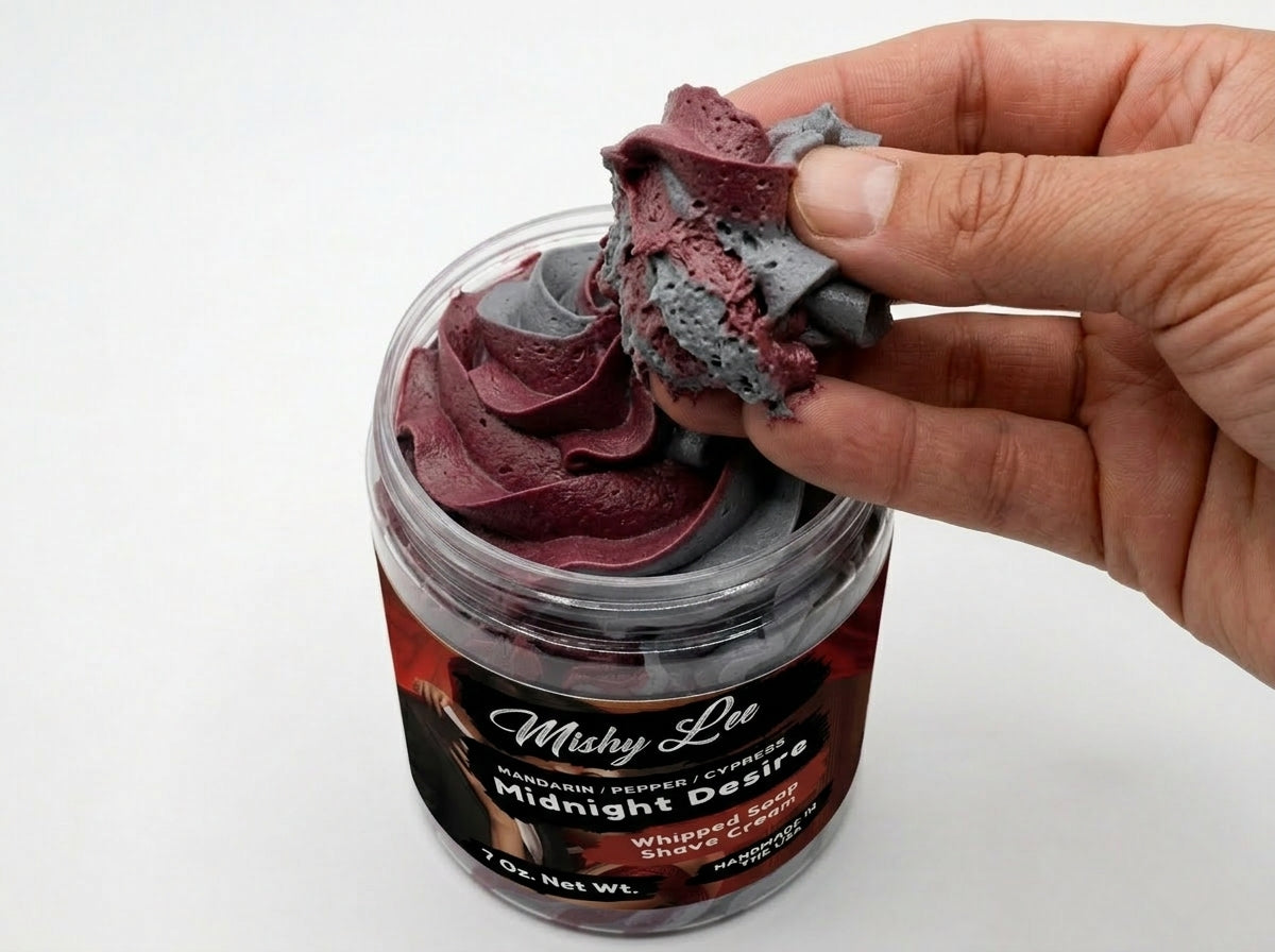 Hand holding maroon and gray whipped shave cream from clear jar