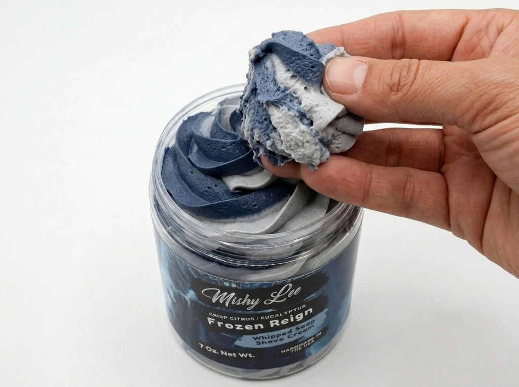 Hand holding a scoop of navy whipped soap from the jar