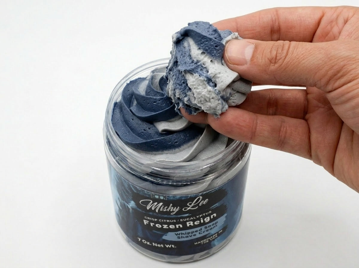 Hand holding a scoop of navy whipped soap from the jar