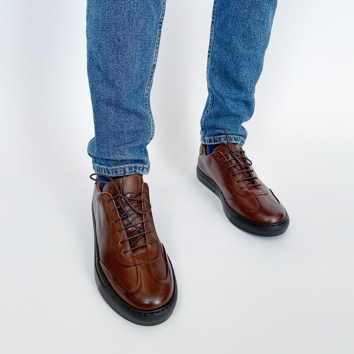 Brown leather lace-up oxford shoes on feet with denim jeans