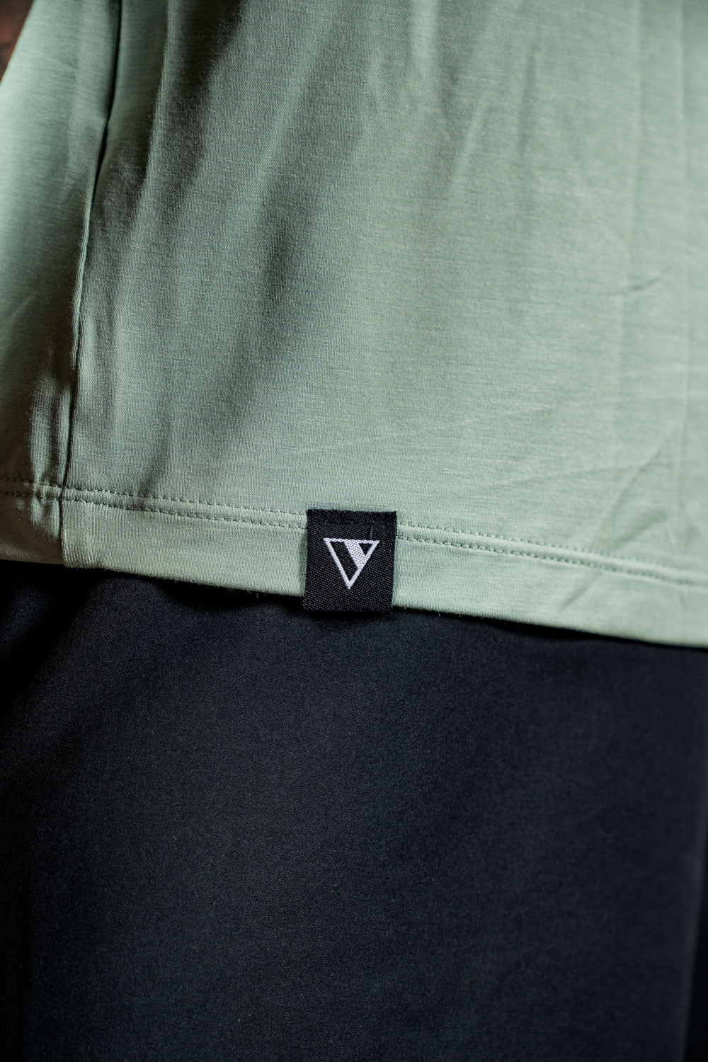 Low-light olive polo hem close-up with small black brand tag near the edge.