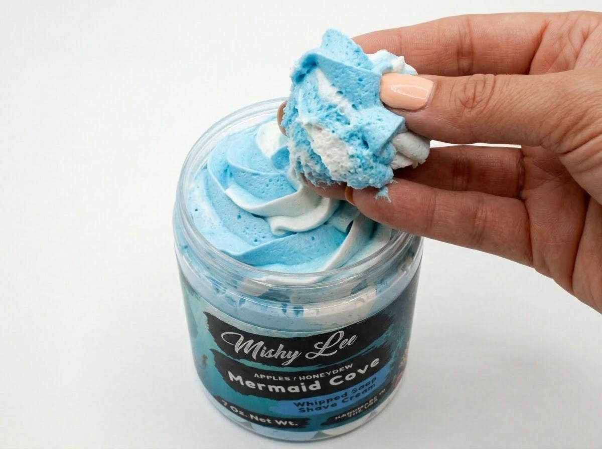 Hand holding a light blue whipped soap scoop above an open jar.