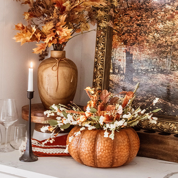Orange metal pumpkin with lid displayed on a tabletop with fall flowers and candles