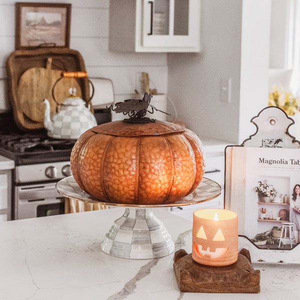 Orange metal pumpkin with dark lid on a pedestal stand, styled for seasonal decor