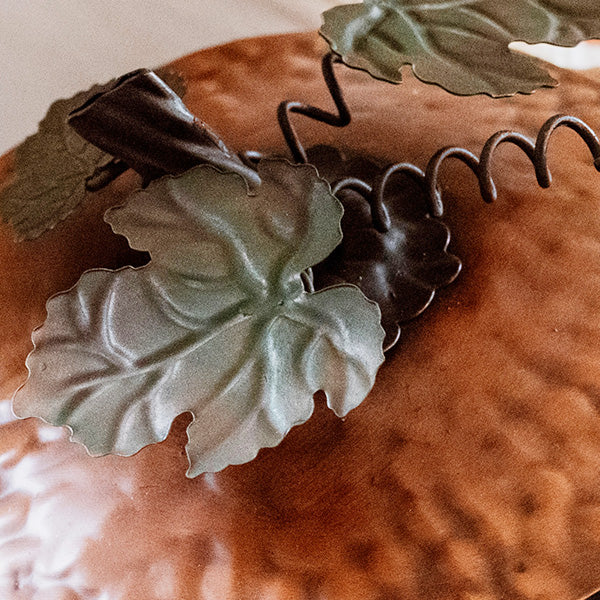 Close-up of embossed orange metal lid with green leaf accents and curled metal detail