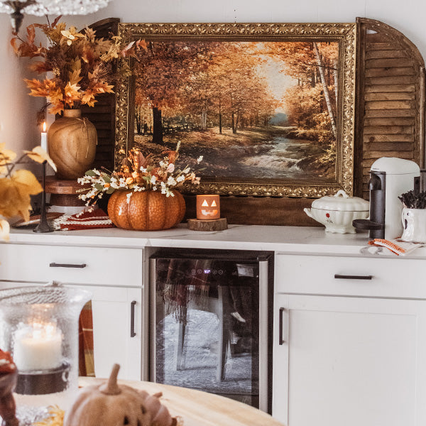 Orange metal pumpkin with lid on a mantel, surrounded by seasonal tabletop decor
