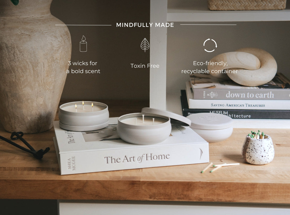Three white candles in round jars on a table, wicks lit