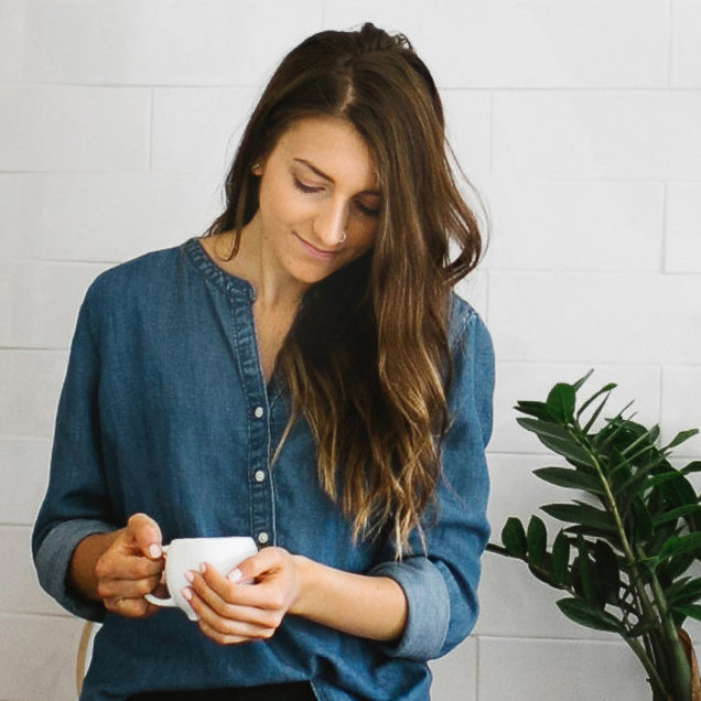 White ceramic teacup with curved handle held by person in a denim shirt
