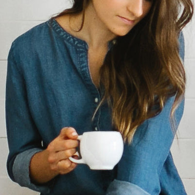 White ceramic teacup held near face by person, curved handle visible