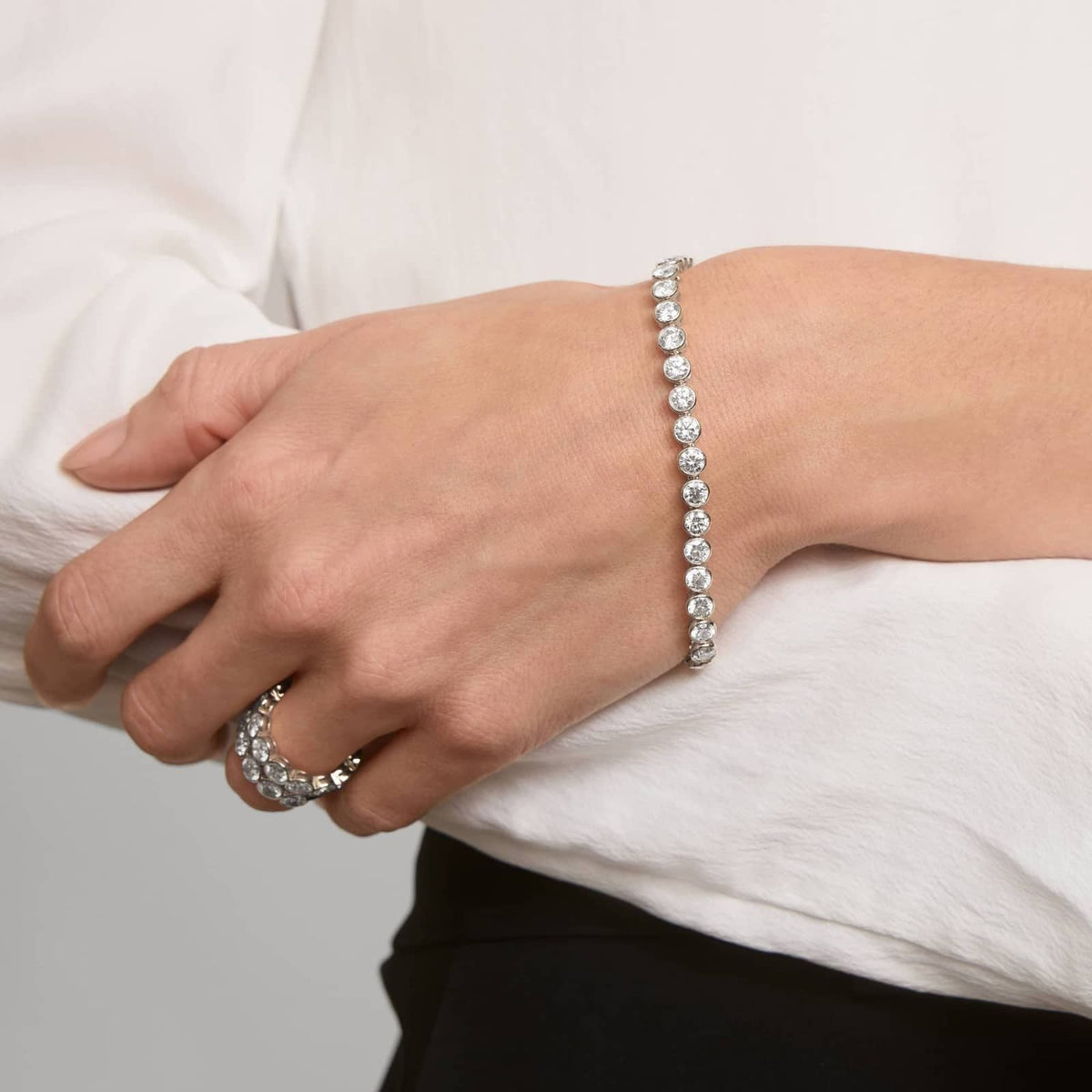 Silver-tone tennis bracelet with bezel-set round stones on a wrist.