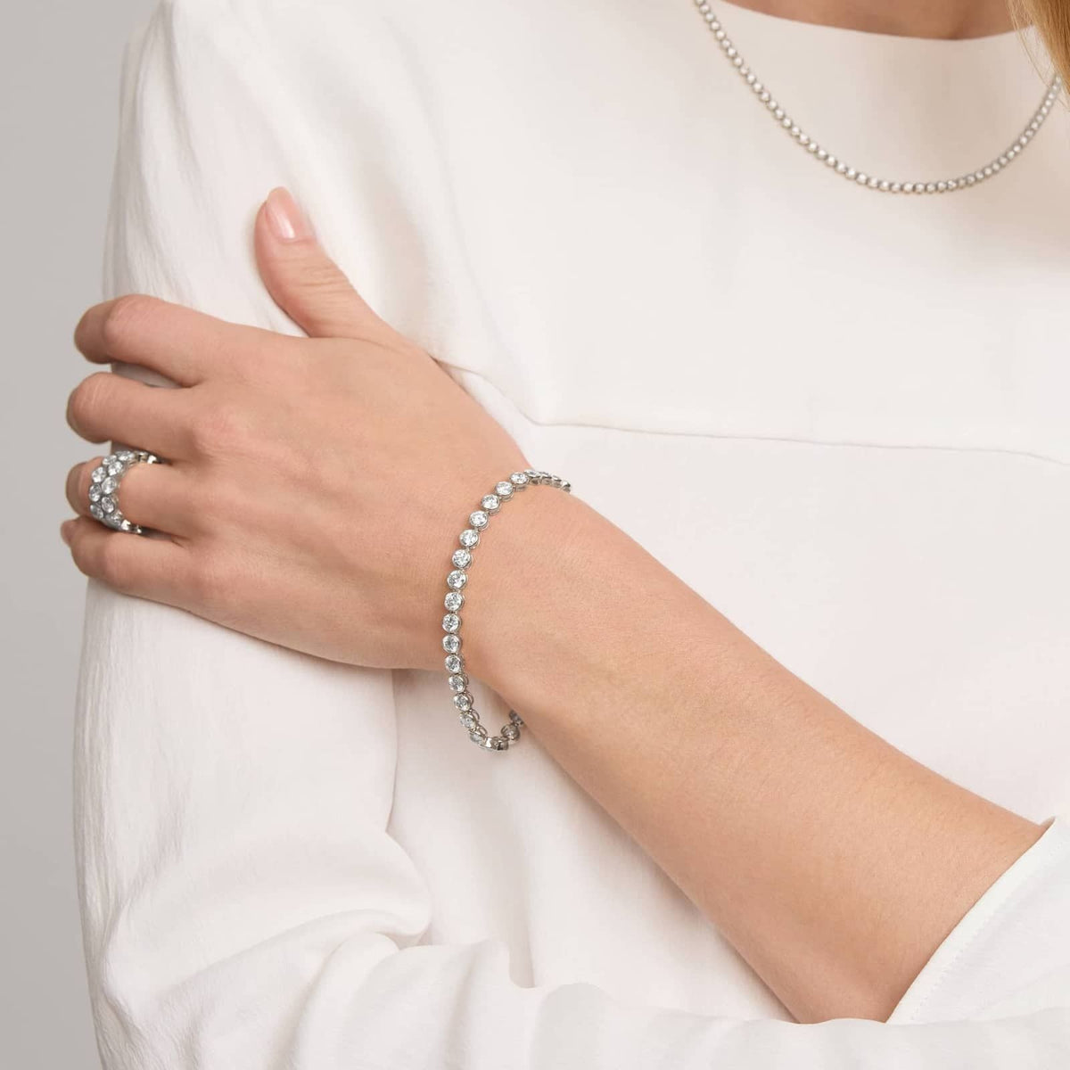 Silver-tone bezel-set round-stone tennis bracelet worn on the forearm.