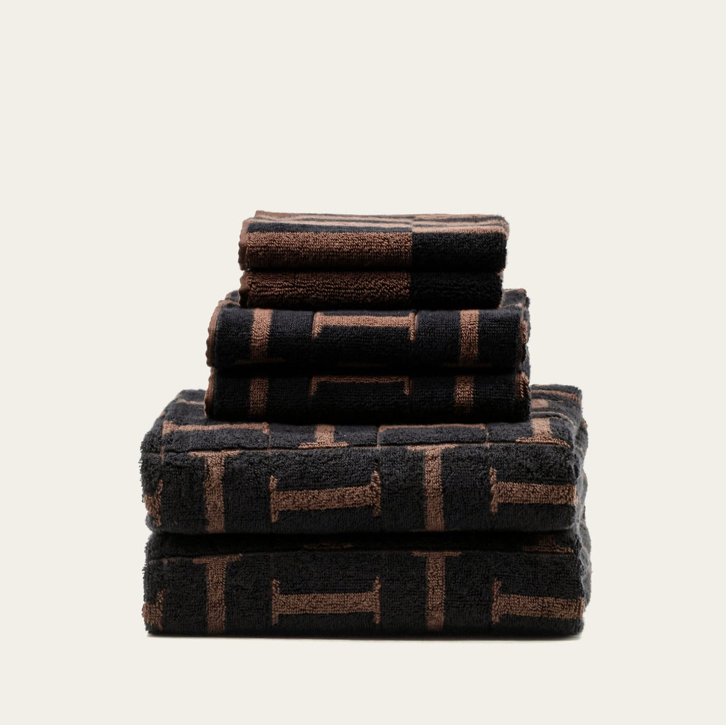 Stack of folded terry cotton towels in tobacco and black with woven geometric pattern